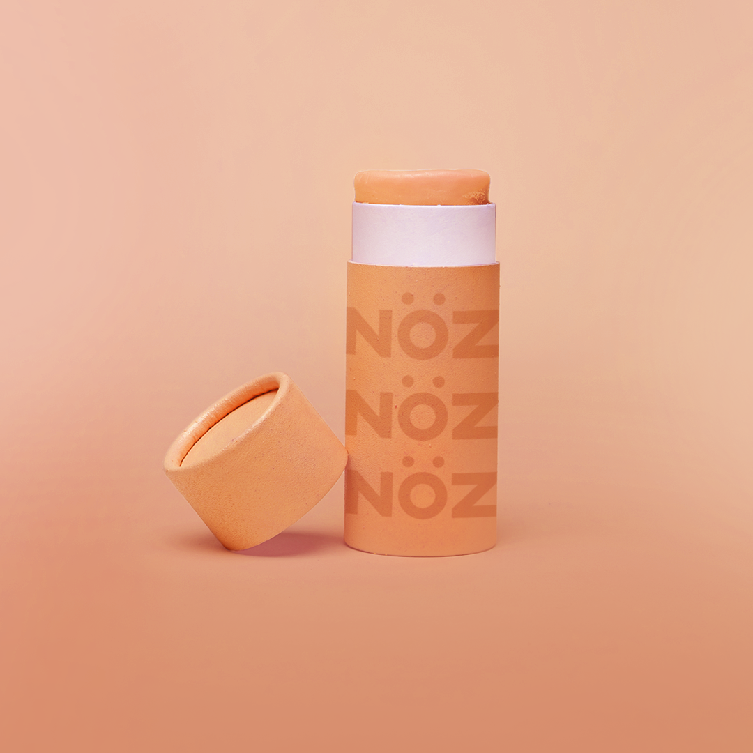 A single orange Nöz sunscreen stick in front of an orange background.